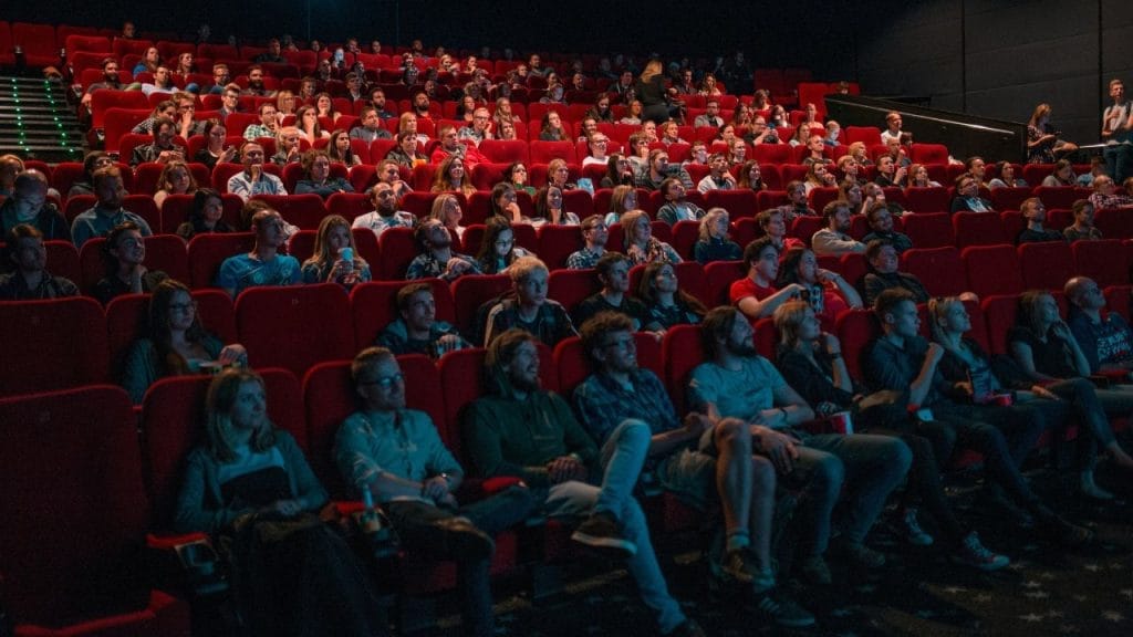 tante persone sedute sui sedili rossi del cinema mentre guardano un film proiettato